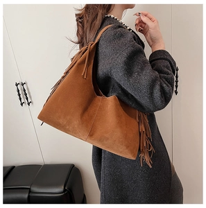 Brown suede tote bag featuring long fringes and wide shoulder strap on a female model
