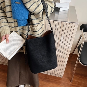 Close-up of black matte suede tote with a wide woven strap shown in a minimalist setting