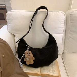 Detail of black crescent shoulder bag with bear pendant on white sofa and vintage book
