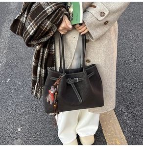 Close-up of black leather tote bag with decorative buckle and bear plush accessory