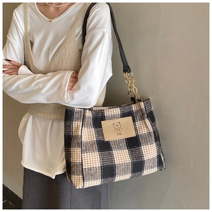 Detail of plaid tote bag showing vintage fabric texture and leather bear logo patch