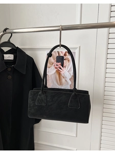 Détail d'un sac sous les bras en daim noir avec de longues anses et une forme rectangulaire