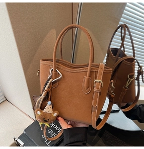 Détail d'un sac seau en daim marron avec surpiqûres blanches et pendentif petit ours