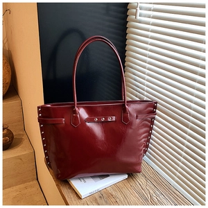 Detail of silver rivets and glossy oil-wax leather texture on a dark red tote bag