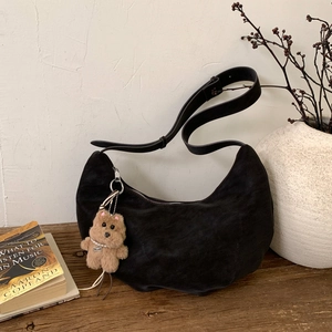 Detailed close-up of a black suede crescent bag with a cute plush dog pendant charm