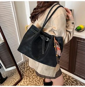 Detail of black suede tote bag with white contrast stitching and teddy bear charm
