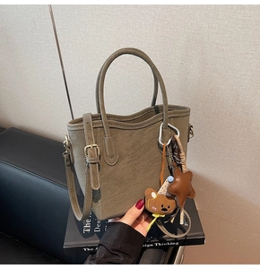 Détail du sac seau vert olive avec breloques étoile et ours sur un livre