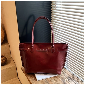 Detail of deep red tote bag with silver studs on a sunny windowsill by the shutters