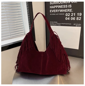 Detail of burgundy suede tote bag with fringe accents on a metallic surface
