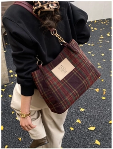 Detail of plaid tote bag with bear patch and chain strap in autumn outdoor setting