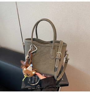Détail du sac seau en cuir kaki avec breloque d'ours et bandoulière réglable pratique