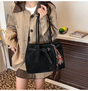 Detail of black leather tote bag with white stitching and bear charm on a shoulder