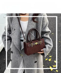 Close-up of dark brown suede crossbody bag with metal ring buckle on grey coat