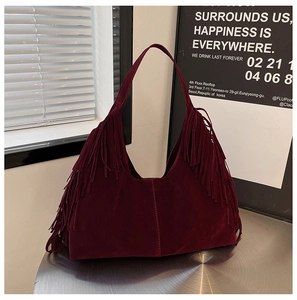 Detail of dark burgundy suede hobo bag with long fringes on metal table