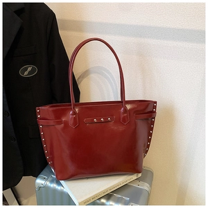 Detail view of burgundy glossy tote bag with silver studs on a silver suitcase