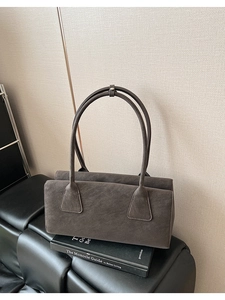 Sac à bandoulière en daim gris foncé minimaliste posé sur une chaise en cuir