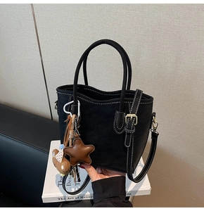 Détail du sac seau noir mat avec surpiqûres blanches contrastées et breloques en peluche