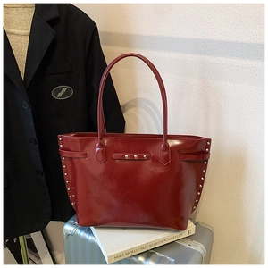 Detail of red rivet tote bag on luggage showing glossy leather texture and silver studs