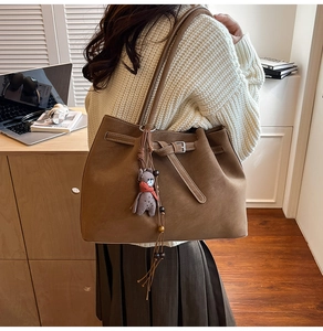 Detail of a brown suede tote bag featuring drawstring belt, silver buckle and plush bear charm