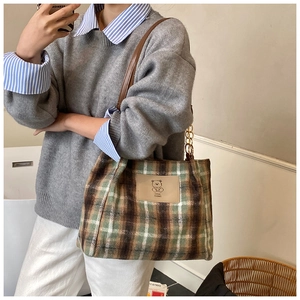 Detail of plaid tote bag featuring leather bear patch and gold chain strap