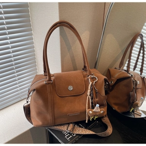 Detail of brown matte leather tote bag featuring a woven strap and plush bear charm