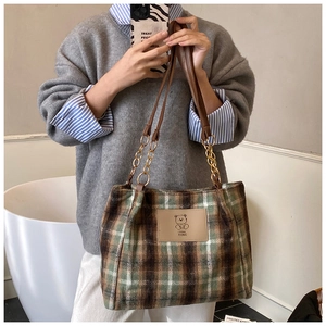 Detail of plaid wool tote bag featuring a leather bear patch and gold chain strap