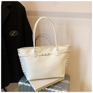 Detail view of cream tote bag with silver rivets placed on a metallic suitcase