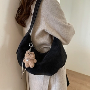 Detail of black suede hobo bag with a plush bear charm on a beige wool coat
