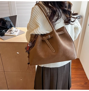 Detail of dark brown leather tote bag with silver buckle and bear pendant in office setting
