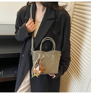 Mini sac seau vert olive avec deux poignées et breloques ours étoile sur blazer noir