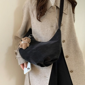Detail of black suede crescent bag with cute teddy bear charm on beige wool coat