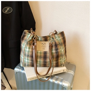 Detail of plaid wool tote bag with leather strap and bear patch on a silver suitcase