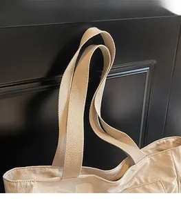 Detail of the wide woven shoulder strap and sturdy stitching on the beige canvas tote bag