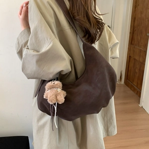 Detail of dark brown crescent shoulder bag with plush bear charm in a cozy setting
