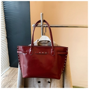 Detail of dark red glossy leather tote bag featuring stylish silver metal rivets on the side