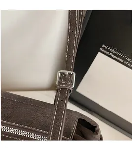 Detail of dark brown leather tote featuring white stitching and silver metal hardware