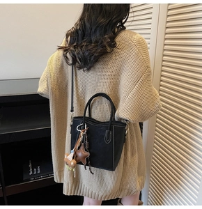 Détails du sac seau noir en cuir avec écusson étoile, charm ours et coutures contrastées