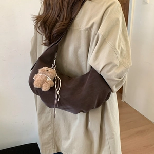 Detail of dark brown crescent bag with a cute plush bear charm on a shoulder strap