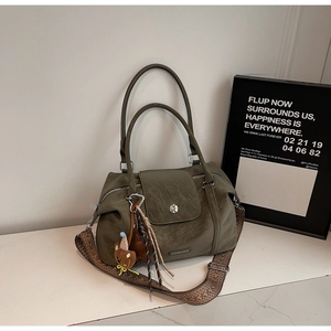 Close-up of olive green vintage leather tote with ethnic woven strap and plush charm