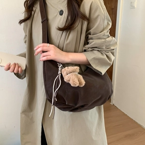 Detail of a large coffee crescent crossbody bag with a plush bear charm on a trench coat