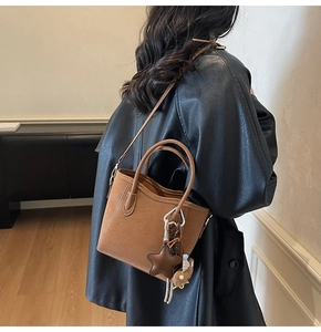 Sac seau caramel avec breloque étoile porté en bandoulière sur un manteau en cuir noir