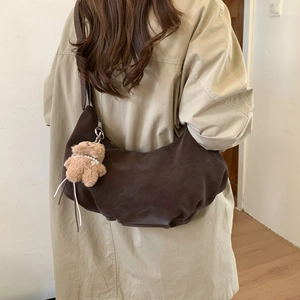 Detailed side view of a dark brown crescent bag with a cute plush bear pendant on a trench coat