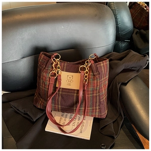 Detail of plaid tote bag featuring a cartoon bear leather patch and golden chain strap