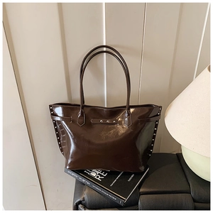 Detailed view of brown glossy leather tote bag with silver rivets on a leather bench