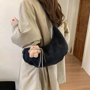 Side view of black crescent shoulder bag with plush bear charm on beige trench coat