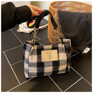 Close-up of checkered tote bag featuring a cartoon bear leather patch and chain strap