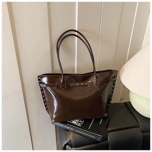 Detail view of the dark brown patent leather tote bag with silver metal rivet accents
