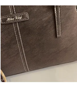 Detail of dark brown faux suede tote bag with contrast white stitching and leather logo patch