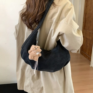 Detail of black crescent crossbody bag with brown plush bear charm and wide shoulder strap