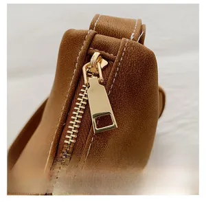 Close-up of golden metal zipper on brown pebble leather bag with white stitching